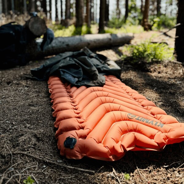 Изолирана надуваема постелка Static V™ Klymit<sup>&reg;</sup> оранжева в леса. Снимка: Rigad