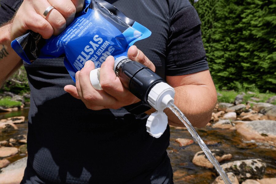 Лицето използва филтър Sawyer squeeze за изтласкване на водата от торба сред природата. Снимка: Rigad