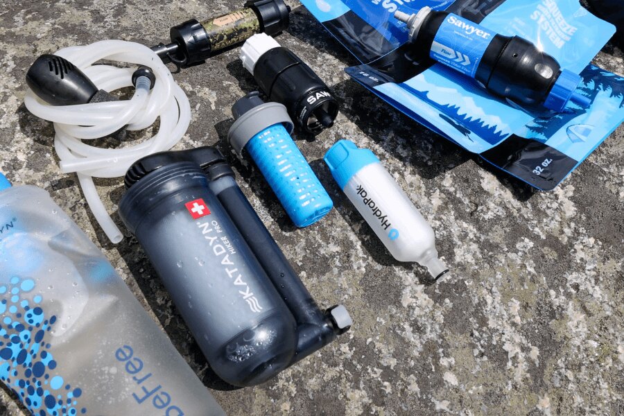 Комплект различни преносими водни филтри Sawyer, HydraPak и Katadyn върху каменна основа. Снимка: Rigad