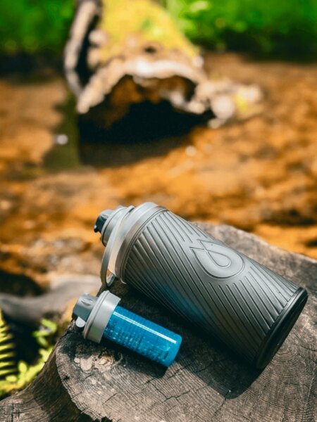 Flux HydraPak бутилка с филтър Cap, поставена върху пън в природата, идеална за пътуване и на открито. Снимка: Rigad