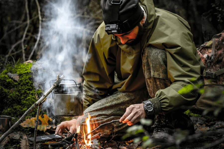 Мъж с мембранно яке до огъня в гората. Източник: https://www.pexels.com/photo/kneeling-man-starting-fire-in-a-fireplace-15538110/