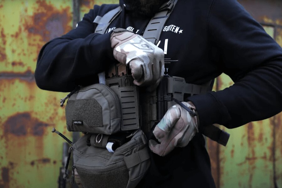 Мъж с Chest Rig Reaper™ Agilite Gear<sup>&reg;</sup>, оборудван с чантички, настройва настройването. Източник: Rigad - видео