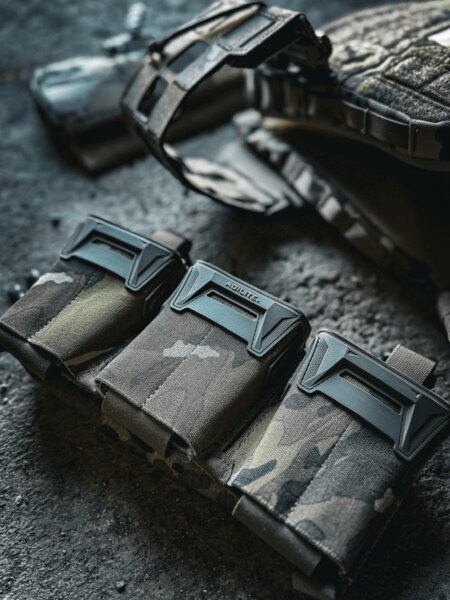 Пинцер Плакат™ Agilite<sup>®</sup> в multicam дизайн, поставен на земята до носача на плочи K-ZERO SF. Снимка: Rigad