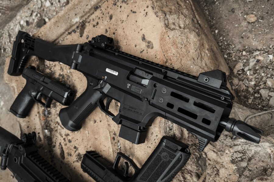 Модерен автомат CZ Scorpion EVO 3 с колиматор и телескопичен приклад, поставен на земята до пистолети и пълнители. Снимка: Rigad