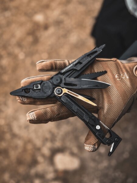 Мултитул Leatherman MUT, намиращ се в дланта с тактическа ръкавица.