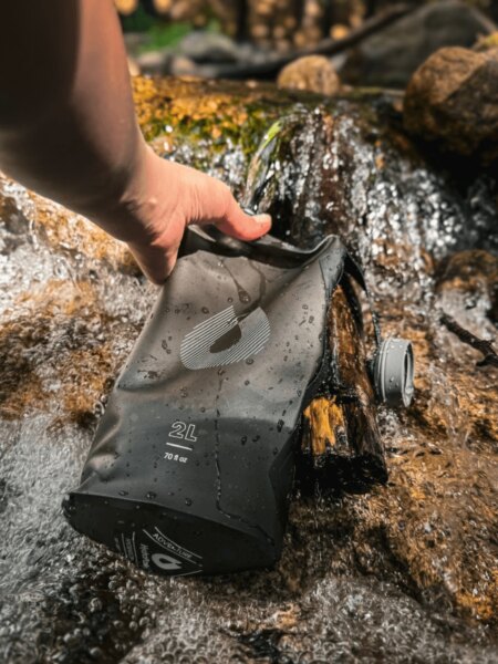 Допълване на запасите от вода в мека хидратираща торба HydraPak от планински поток.
