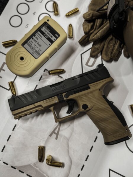 Пистолет "Walther PDP Full Size" с таймер за стрелба, патрони и ръкавици, поставен върху мишена.