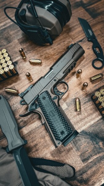 Пистолет "Schmeisser HUGO 1911 5" в калибър .45 ACP поставен на масата с боеприпаси и стрелково оборудване.